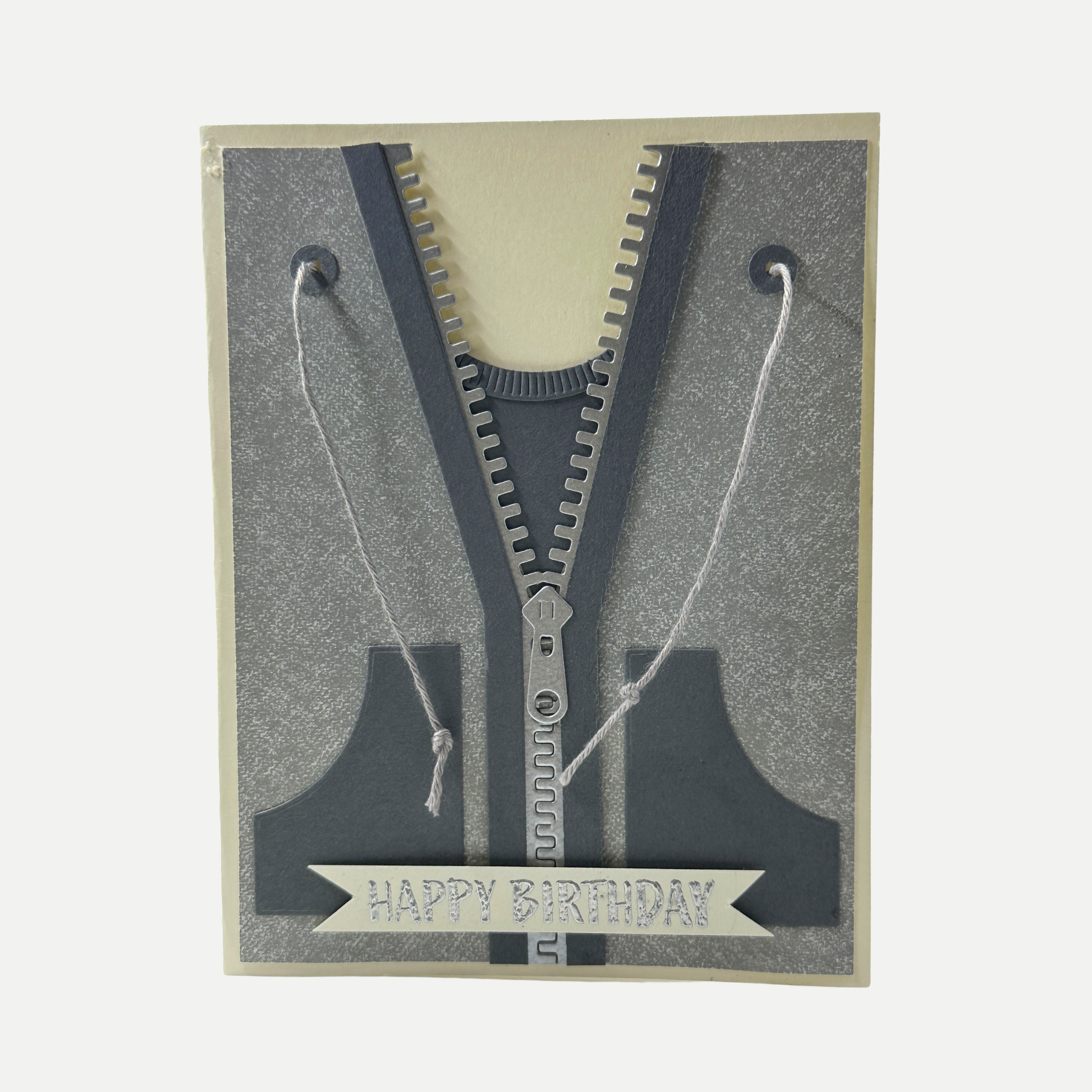A handmade zip-card birthday gift featuring a 3D zipper design with gray glitter paper, dark gray layers, white string loops, and a 'HAPPY BIRTHDAY' banner at the bottom.