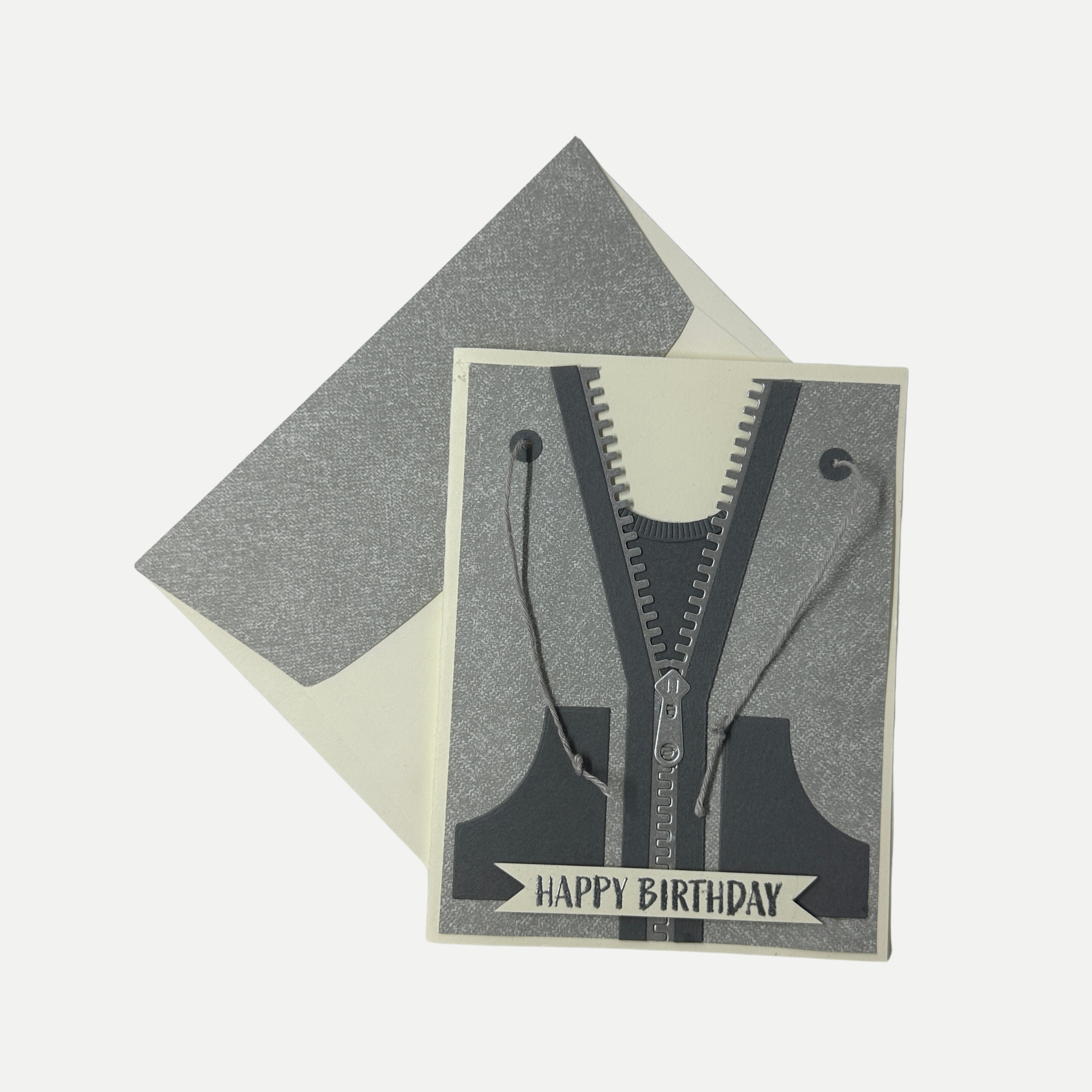 A square birthday card featuring a zipper hoodie design with the words 'HAPPY BIRTHDAY' at the bottom, shown with a matching envelope on a light gray background.